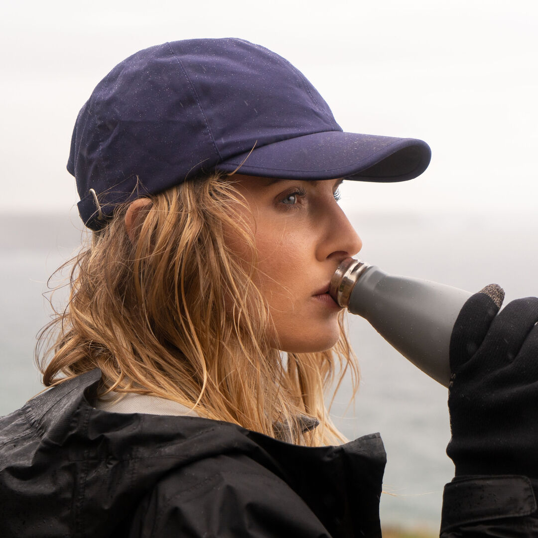 primary lady wearing sealskinz waterproof all weather cap drinking water bottle